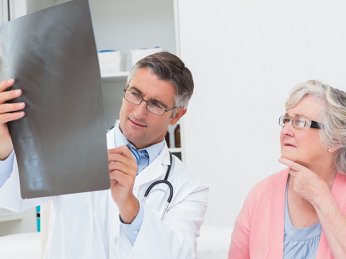 Arzt und Patientin betrachten Röntgenaufnahme der Wirbelsäule