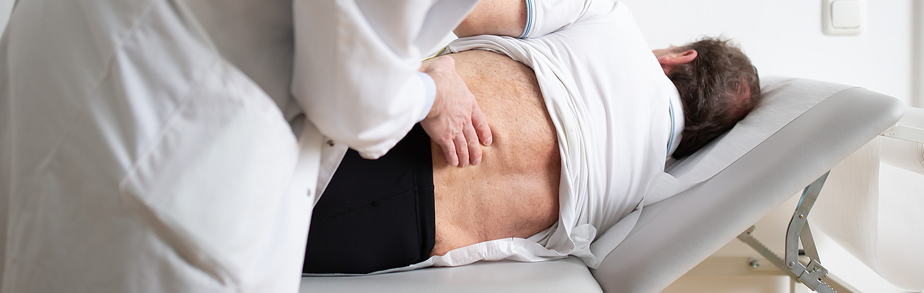 Dr. Buchmann untersucht den Rücken eines Patienten.