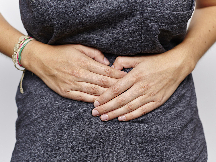 Junge Frau hält beide Hände auf schmerzenden Bauch